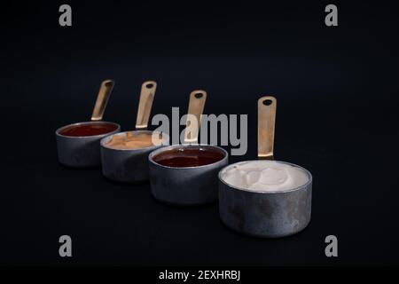 Eine Nahaufnahme von kleinen Pfannen mit verschiedenen Saucen auf Schwarzer Hintergrund Stockfoto