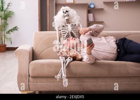 Alter Mann sitzt auf dem Sofa mit dem weiblichen Skelett In unsterbst Liebe Konzept Stockfoto