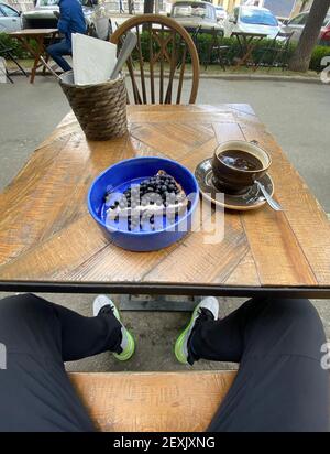 Von oben Keramikschale mit Scheibe Käsekuchen gekrönt Mit Heidelbeeren und großer Tasse Tee auf Holztisch Stockfoto