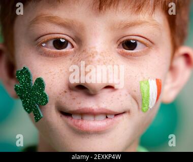 Nahaufnahme von lächelndem Kind mit der tricolor irischen Flagge des heiligen patricks und einem Kleeblatt auf dem Kindergesicht während der Festivalfeier mit Kopierfläche. Stockfoto