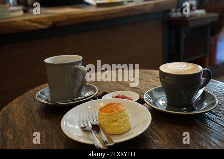 Eine Tasse heißen schwarzen Kaffees mit Butter serviert Schlichte Scone und Beerenmarmelade auf Holztisch Stockfoto