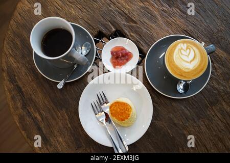 Eine Tasse heißen schwarzen Kaffees mit Butter serviert Schlichte Scone und Beerenmarmelade auf Holztisch Stockfoto