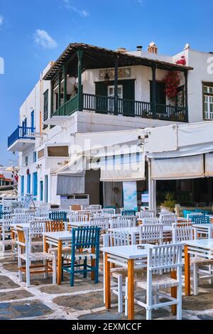 Café oder Restaurant im Freien in einer typisch griechischen Inselstadt. Kirche, blaue Kuppel, Touristen durchstreifen. Sonniger Sommertag, Mykonos, Kykladen, Griechenland. Vertikale Aufnahme Stockfoto