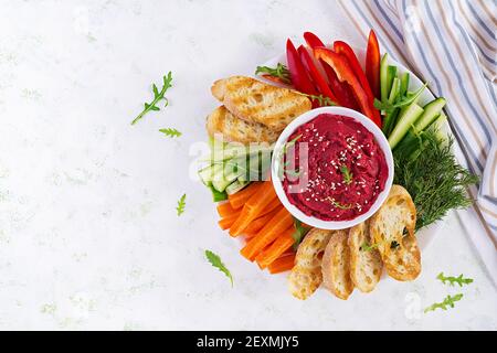 Gerösteter Rübenhummus mit Toast und Gemüse auf hellem Hintergrund. Beetroot Hummus. Draufsicht, oben, Kopierbereich Stockfoto