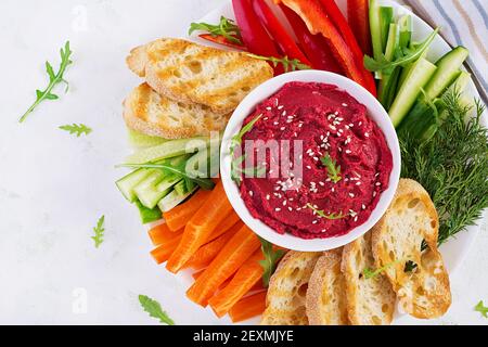 Gerösteter Rübenhummus mit Toast und Gemüse auf hellem Hintergrund. Beetroot Hummus. Draufsicht, oben, Kopierbereich Stockfoto