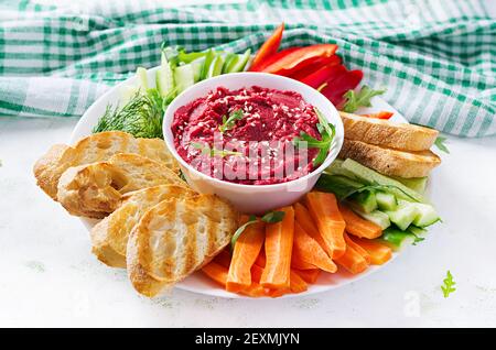 Gerösteter Rübenhummus mit Toast und Gemüse auf hellem Hintergrund. Beetroot Hummus. Stockfoto