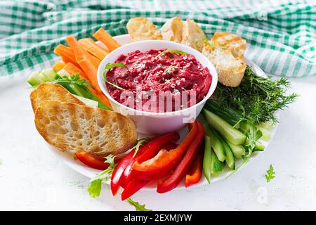 Gerösteter Rübenhummus mit Toast und Gemüse auf hellem Hintergrund. Beetroot Hummus. Stockfoto