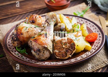 Gebackene Hähnchenschenkel mit Kartoffelscheiben und Kräutern. Barbecue Hähnchendrumsticks auf Holztisch. Stockfoto