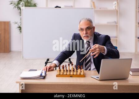 Alter Geschäftsmann Angestellter, der Schach am Arbeitsplatz spielt Stockfoto