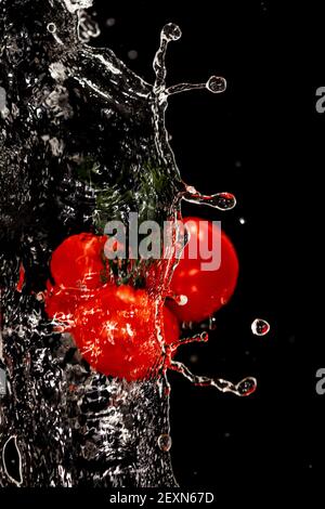 Ein Bündel von drei roten reifen Tomaten hinter einem Wasserspritzer auf schwarzem Hintergrund. Hochwertige Fotos Stockfoto