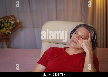 Der 50-jährige Mann hört zu Hause Musik auf Kopfhörern, sitzt auf einem Stuhl. Erholsame Freude. Stockfoto