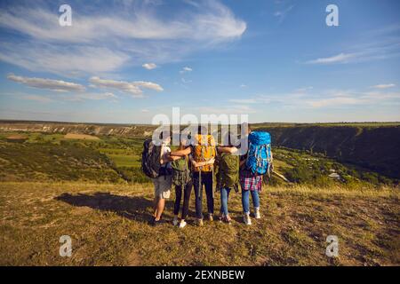 Gruppe von Wanderern mit Rucksäcken stehen auf der Bergspitze und beobachten Landschaft, Rückansicht. Junge Freunde auf Campingausflug Stockfoto