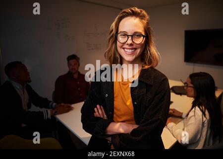 Porträt einer lächelnden jungen selbstbewussten Geschäftsfrau vor Ihre Kollegen sitzen am Schreibtisch Stockfoto