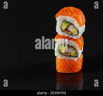Balancieren von frischen Sushi-Rollen auf schwarzem Hintergrund mit Spiegelung. Japanische Küche Stockfoto