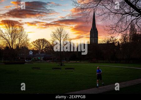 Salisbury, Großbritannien. März 2021, 5th. Ein Jogger geht durch die Queen Elizabeth Gardens mit der Salisbury Cathedral hinter sich, wenn die Sonne aufgeht. Fotograf: Matthew Lofthouse/Alamy Live News Stockfoto