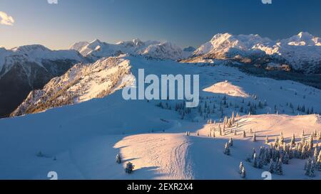 Luftaufnahme der Winterlandschaft mit schneebedecktem Wald in den Bergen mit schönem Sonnenuntergangslicht. Stockfoto