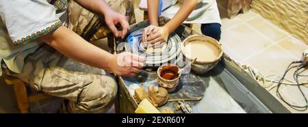 Die Hände eines Meisters und eines Studenten machen einen Krug auf einem Potter-Rad aus gelbem Ton. Selektive Fokussierung auf die Hände Stockfoto