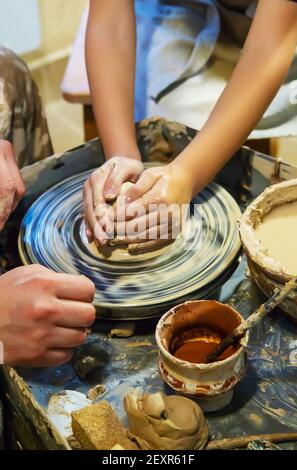 Die Hände eines Meisters und eines Studenten machen einen Krug auf einem Potter-Rad aus gelbem Ton. Selektive Fokussierung auf die Hände Stockfoto