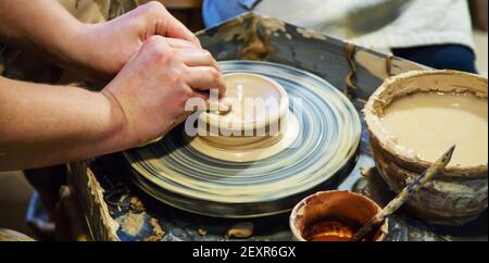 Die Hände eines Meisters und eines Studenten machen einen Krug auf einem Potter-Rad aus gelbem Ton. Selektive Fokussierung auf die Hände Stockfoto