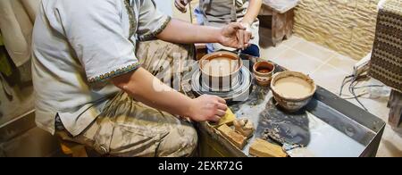 Die Hände eines Meisters und eines Studenten machen einen Krug auf einem Potter-Rad aus gelbem Ton. Selektive Fokussierung auf die Hände Stockfoto
