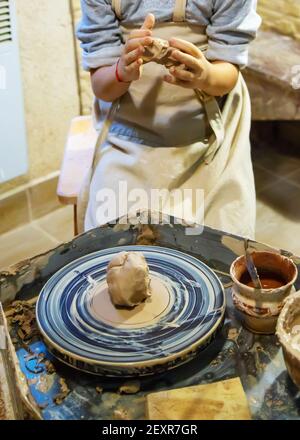 Die Hände eines Meisters und eines Studenten machen einen Krug auf einem Potter-Rad aus gelbem Ton. Selektive Fokussierung auf die Hände Stockfoto