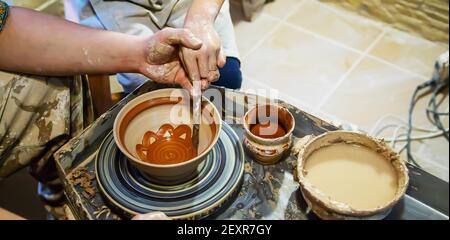 Die Hände eines Meisters und eines Studenten machen einen Krug auf einem Potter-Rad aus gelbem Ton. Selektive Fokussierung auf die Hände Stockfoto