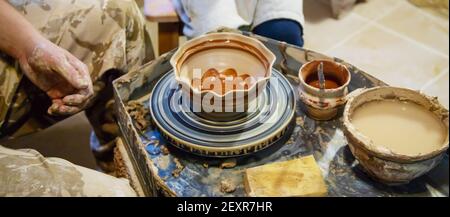 Die Hände eines Meisters und eines Studenten machen einen Krug auf einem Potter-Rad aus gelbem Ton. Selektive Fokussierung auf die Hände Stockfoto