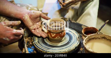 Die Hände eines Meisters und eines Studenten machen einen Krug auf einem Potter-Rad aus gelbem Ton. Selektive Fokussierung auf die Hände Stockfoto