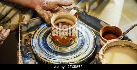 Die Hände eines Meisters und eines Studenten machen einen Krug auf einem Potter-Rad aus gelbem Ton. Selektive Fokussierung auf die Hände Stockfoto