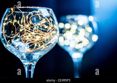 Gin Glas mit Feenlicht im Inneren mit einem anderen im Hintergrund verschwommen, helle Lichter in einem glänzenden Glas vor schwarzem Hintergrund, launisch und stilvoll Stockfoto