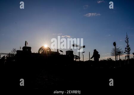 Berlin, Deutschland. März 2021, 05th. Die Sonne geht hinter der Kuppel des Reichstagsgebäudes auf, als ein Passant durch das Regierungsviertel geht. Quelle: Christoph Soeder/dpa/Alamy Live News Stockfoto