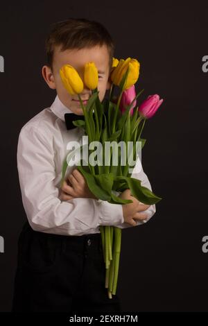 Der Junge mit Vitiligo in einem weißen Hemd und ein Fliege mit Tulpen auf schwarzem Studio-Hintergrund Stockfoto