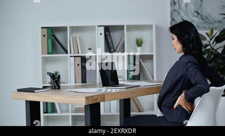 Seitenansicht einer Geschäftsfrau mit Rückenschmerzen im Büro Stockfoto