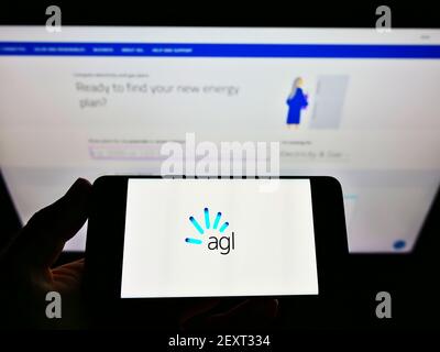 Person mit Mobiltelefon und Logo des australischen Energieversorgers AGL Energy Limited auf dem Bildschirm vor der Webseite. Fokus auf Handy-Display. Stockfoto