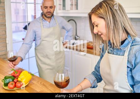 Pärchen in der Küche, die Essen zubereitet. Sie bereitet ein Glas Wein zu, während er ihr zuschaut. Hochwertige Fotos Stockfoto