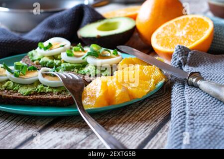 Offenes Sandwich mit Avocado und gekochten, in Scheiben geschnittenen Eiern serviert Frisches Obst auf einer Bambusplatte auf dem Küchentisch bei Zu Hause Stockfoto