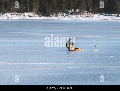 Angler Angeln auf dem Eis eines gefrorenen Sees an einem klaren Wintertag. Stockfoto