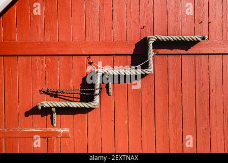 Treppe steigt nach oben aus einem Seil auf rotem Holzhintergrund aus Holzplanken Muster erstellt. Das Detail der Fassade des roten Hauses stellt die aufrassenden Stufen dar Stockfoto