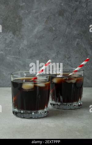 Cola-Gläser auf weißem strukturiertem Tisch vor grauem Hintergrund Stockfoto