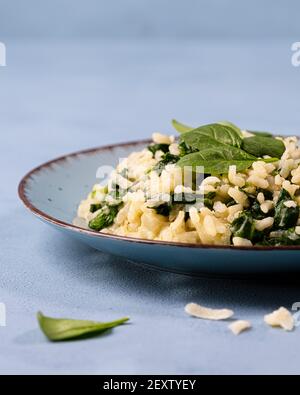 Risotto mit jungen Spinatblättern auf einem petrolfarbenen Teller mit Serviette, dekoriert mit frischen Spinatblättern Stockfoto