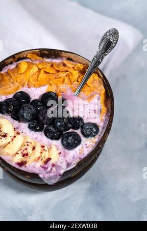 Kokosnussschale gefüllt mit Heidelbeer-Joghurt mit frischen Bananen, Heidelbeeren und Cornflakes Stockfoto