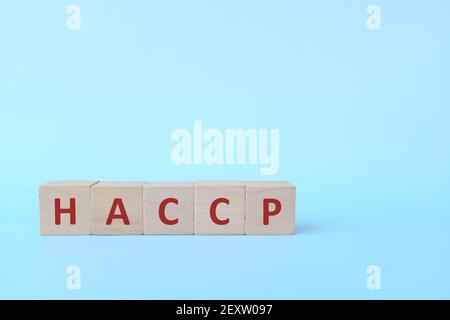 HACCP Akronym in Holzblöcken auf blauem Hintergrund. Sicherheit in der Lebensmittelindustrie und Fertigungskonzept. Stockfoto