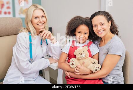 Glückliche afroamerikanische Mutter mit ihrer Tochter beim Besuch eines Kinderarztes. Gesundheit von Kindern Stockfoto