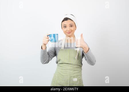 Bild einer lächelnden jungen Frau im Vorfeld mit einem Blaue Tasse mit Daumen nach oben Stockfoto