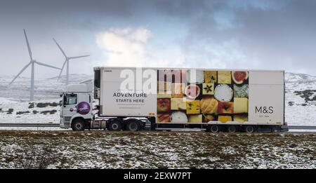 Auf der Autobahn M6 fahren Waggons Richtung Süden durch Cumbria bei der Kreuzung 37, im Hintergrund der Windpark Lambriggs. Cumbria, Großbritannien. Stockfoto