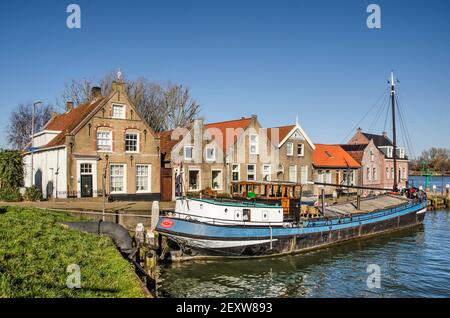 Puttershoek, Niederlande, 26. Februar 2021: Historische Häuser und ein Binnenschiff im kleinen Hafen der Stadt mit dem Fluss Oude Maas im Hintergrund Stockfoto