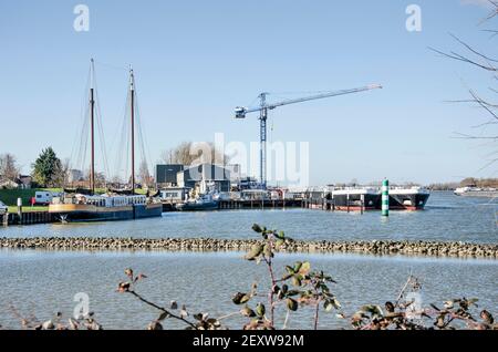 Puttershoek, Niederlande, 26. Februar 2021: Blick auf die Uferpromenade der Stadt mit verschiedenen Schiffen, kleinen Industrien und dem Fluss Oude Maas Stockfoto