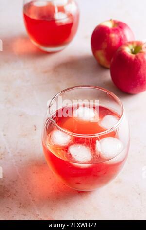 Zwei Gläser Pink Lady Apfelgetränk mit Eiswürfeln und zwei frische Äpfel im Hintergrund. Stockfoto
