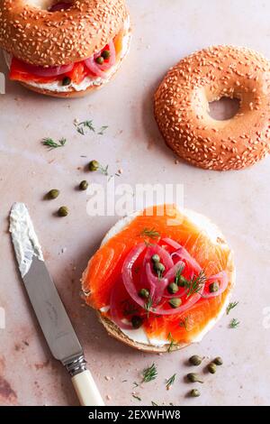 Bagel zur Hälfte mit Frischkäse und gekrönt mit geräucherter Forelle, eingelegten roten Zwiebeln, Kapern und Dill. Stockfoto