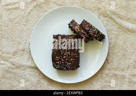 Hausgemachter Kakao-Kuchen mit Schokoladenvereisung und bunten Streuseln, auf einem weißen Porzellanteller platziert Stockfoto